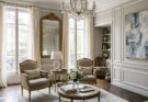 Elegant Parisian chic living room with muted linen fauteuil chairs, gold leaf mirrors, a crystal chandelier, and abstract art.