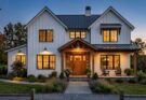 Modern farmhouse exterior with white board-and-batten, black windows, wood accents, and gooseneck barn lights.