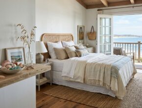 Coastal bedroom with a rattan headboard, jute rug, linen bedding, driftwood accents, and a shell collection on a shelf.