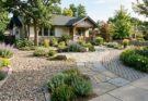 A low-maintenance front yard design with flagstone patio, permeable paver pathway, and decorative gravel.