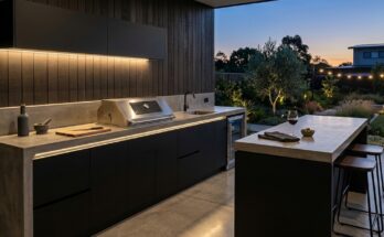 Modern minimalist outdoor kitchen with polished concrete, matte black cabinets, stainless steel grill, and warm LED lighting.