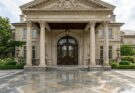 Grand estate portico with polished granite flooring and oversized double doors with intricate glasswork.