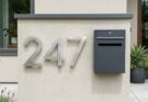 Modern oversized house numbers in brushed metal and a designer mailbox, enhancing a custom exterior facade.